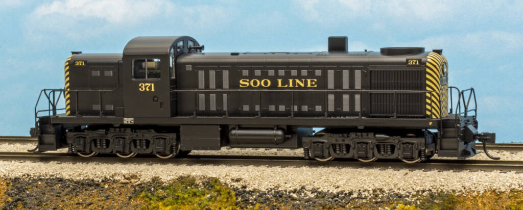 Color photo of HO scale locomotive painted black and yellow on scenicked base with a sky blue backdrop. 