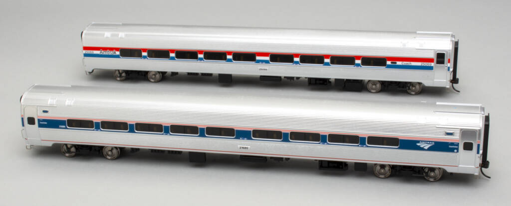 Color photo of two HO scale fluted-side passenger coaches with simulated stainless steel finish and red, white, and blue graphics on gray background. 