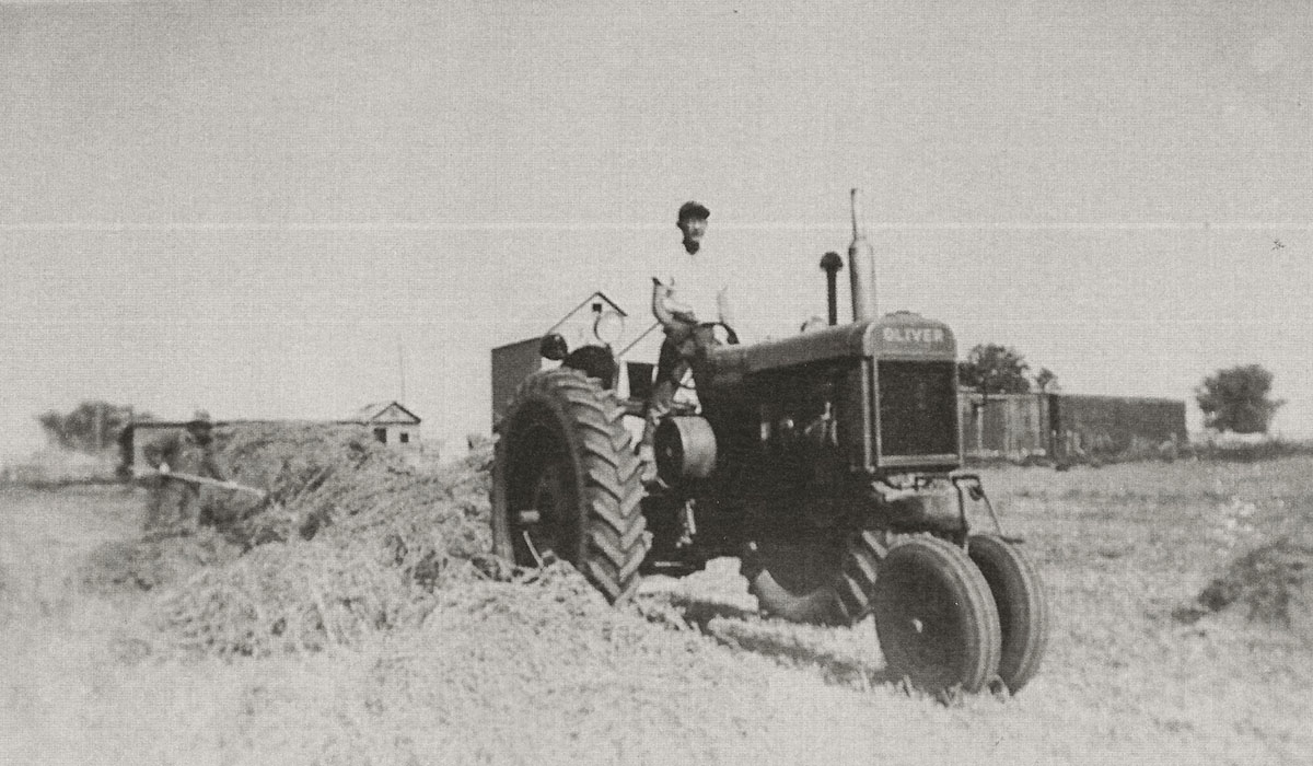 Young man driving a 1940s farm tractor. Restoring a World War II boxcar home.