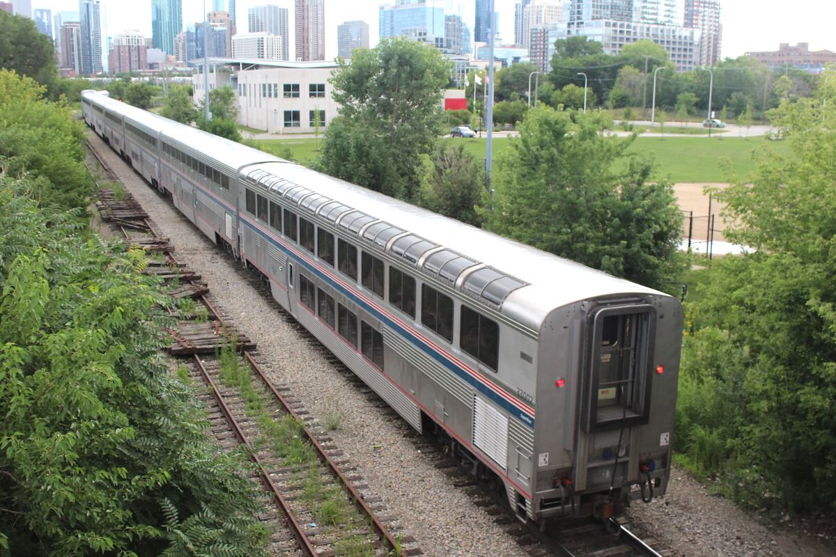 Going-away shot of passenger train with bilevel cars, with Chicago skyline in distance
