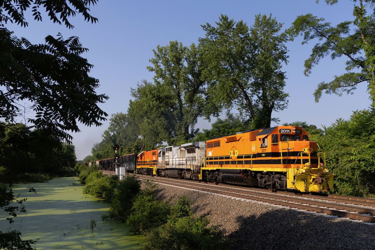 Train with two orange and black locomotives sandwiching one gray and white unit