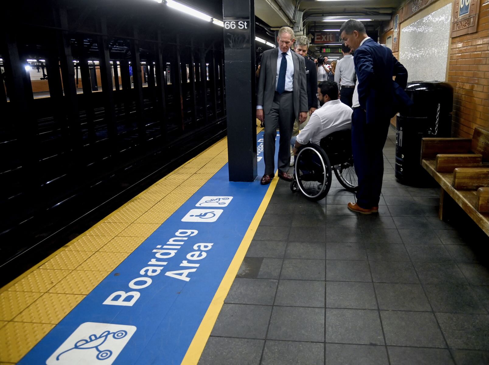 Men looking at subway platform marked as a boarding area for those in wheelchairs or with strollers
